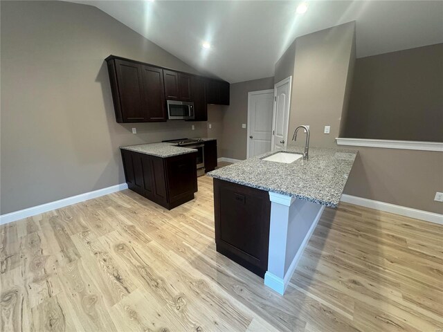 kitchen with light stone counters, a sink, light wood-style flooring, stainless steel appliances, and lofted ceiling