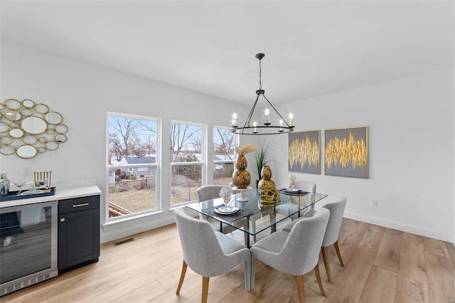 dining area with visible vents, an inviting chandelier, beverage cooler, baseboards, and light wood finished floors
