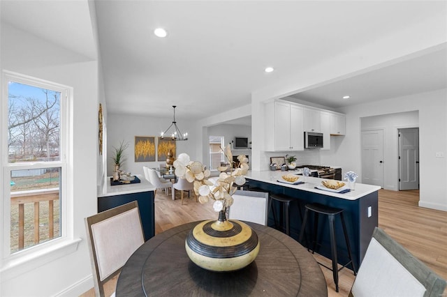 kitchen featuring white cabinets, light countertops, stainless steel microwave, baseboards, and light wood-type flooring