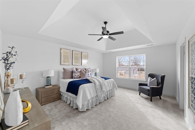 bedroom with baseboards, a ceiling fan, a tray ceiling, and light carpet