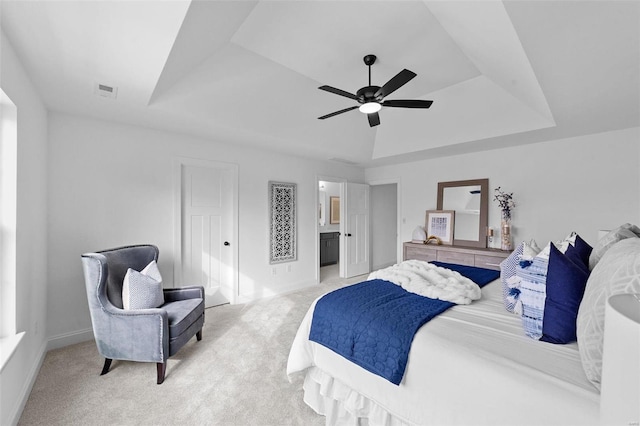 bedroom featuring ceiling fan, light colored carpet, baseboards, ensuite bathroom, and a tray ceiling