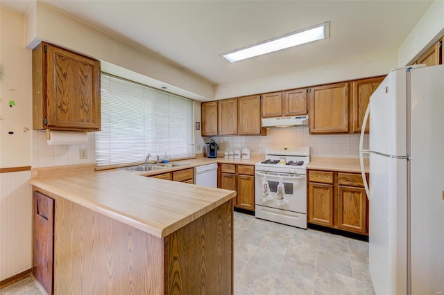 kitchen with a peninsula, a sink, white appliances, under cabinet range hood, and decorative backsplash