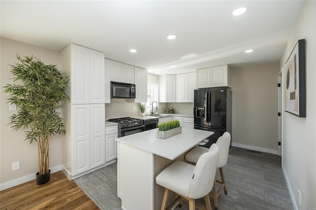 kitchen featuring white cabinetry, baseboards, wood finished floors, a kitchen bar, and black appliances