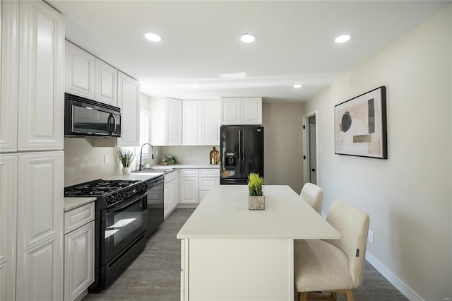 kitchen featuring a center island, wood finished floors, a sink, black appliances, and a breakfast bar