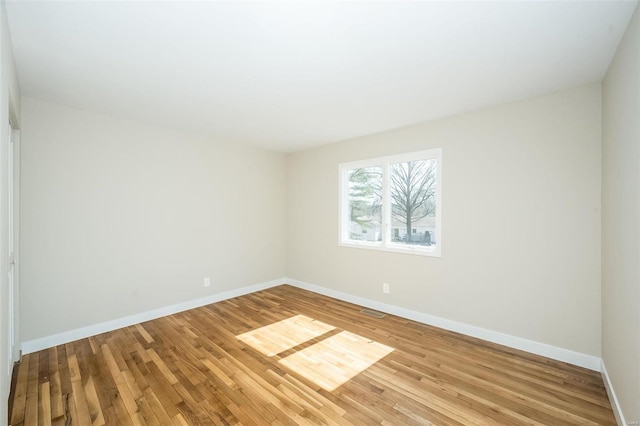 spare room with baseboards, visible vents, and wood finished floors