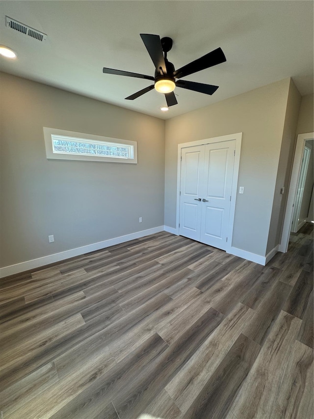 unfurnished bedroom featuring a closet, wood finished floors, visible vents, a ceiling fan, and baseboards