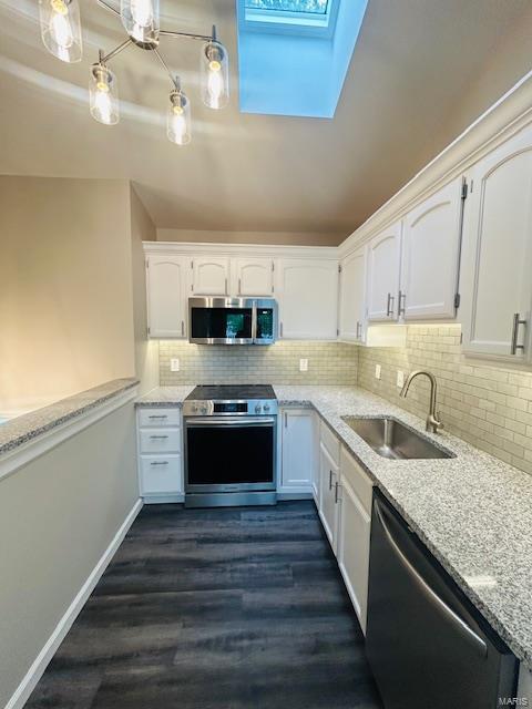 kitchen with white cabinets, tasteful backsplash, a sink, appliances with stainless steel finishes, and a skylight