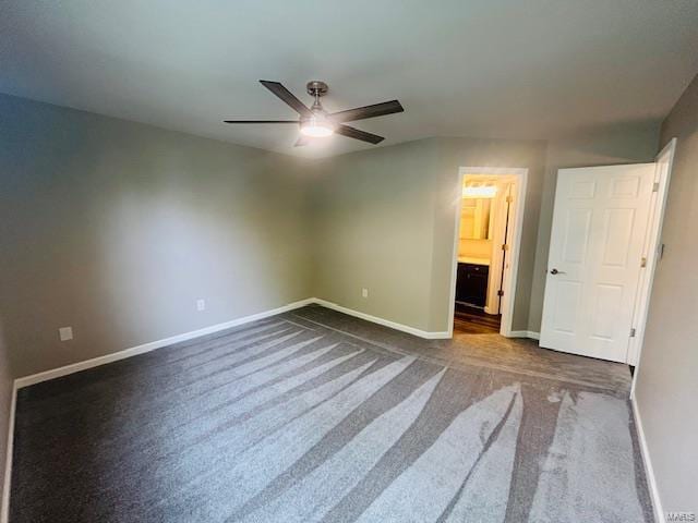 unfurnished bedroom featuring baseboards, ensuite bathroom, ceiling fan, and dark colored carpet