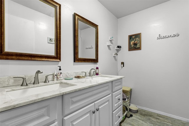 bathroom with a sink, baseboards, double vanity, and wood finished floors