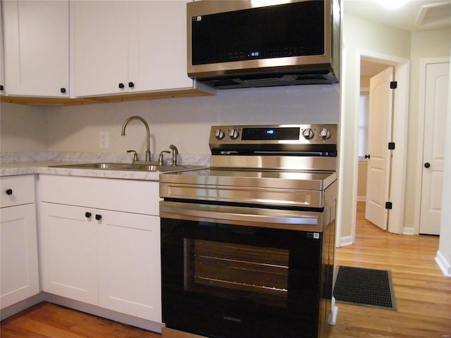 kitchen featuring white cabinets, appliances with stainless steel finishes, a sink, and light wood-style flooring