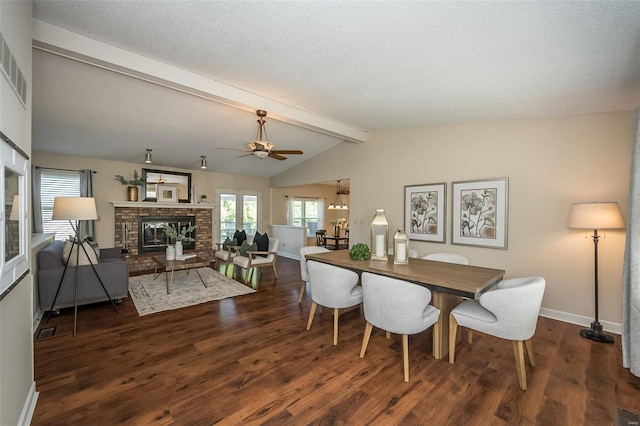 dining space with a ceiling fan, a brick fireplace, wood finished floors, baseboards, and lofted ceiling with beams