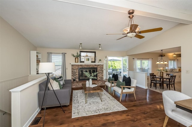 living room with ceiling fan, visible vents, a brick fireplace, dark wood-style floors, and vaulted ceiling with beams