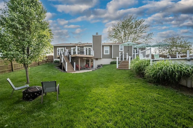 rear view of property featuring a fire pit, a wooden deck, fence, stairs, and a yard