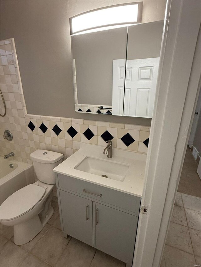 bathroom with vanity, toilet, tile walls, a wainscoted wall, and shower / washtub combination
