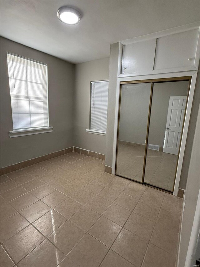 unfurnished bedroom with a closet, baseboards, tile patterned floors, and visible vents