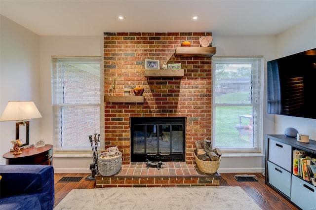living area with visible vents, wood finished floors, baseboards, and a brick fireplace