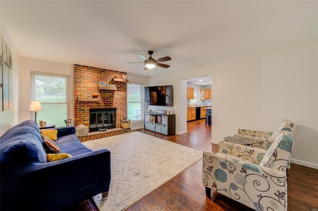 living area featuring plenty of natural light, dark wood-style flooring, a ceiling fan, and a brick fireplace