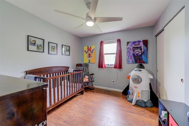 bedroom featuring a closet, wood finished floors, a nursery area, ceiling fan, and baseboards