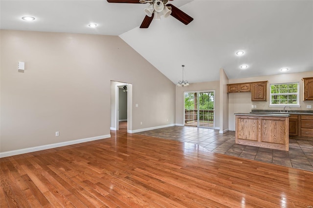 unfurnished living room with wood finished floors, ceiling fan with notable chandelier, a sink, high vaulted ceiling, and baseboards