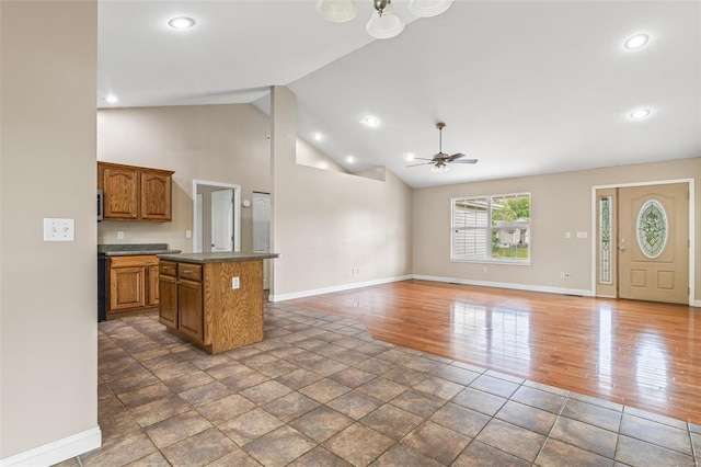 kitchen featuring wood finished floors, a ceiling fan, brown cabinets, dark countertops, and a kitchen island