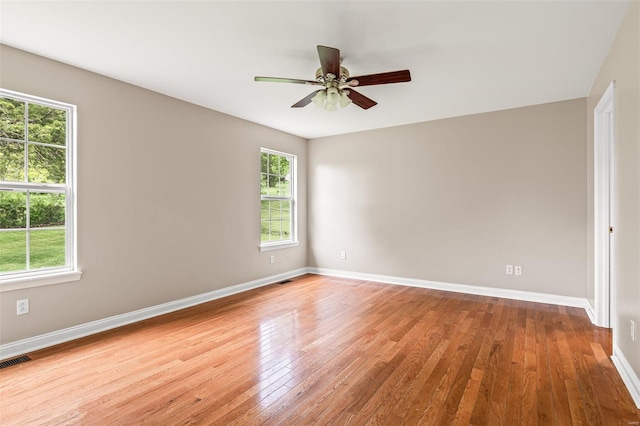 empty room featuring a ceiling fan, visible vents, wood finished floors, and baseboards