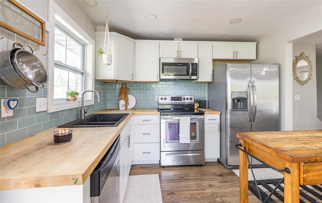 kitchen featuring appliances with stainless steel finishes, a sink, wood counters, dark wood finished floors, and decorative backsplash