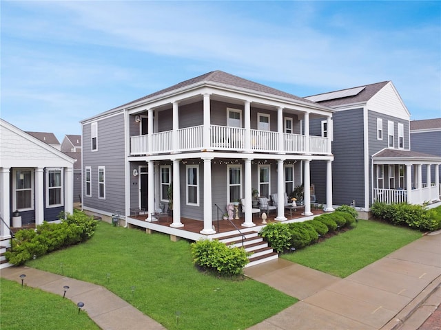 greek revival inspired property with a porch, a balcony, and a front lawn