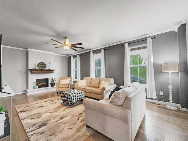 living area featuring a large fireplace, ornamental molding, a ceiling fan, and wood finished floors