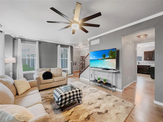 living area featuring crown molding, stairs, light wood-style flooring, and baseboards