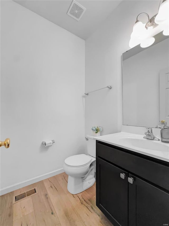 half bath with visible vents, wood finished floors, toilet, and vanity