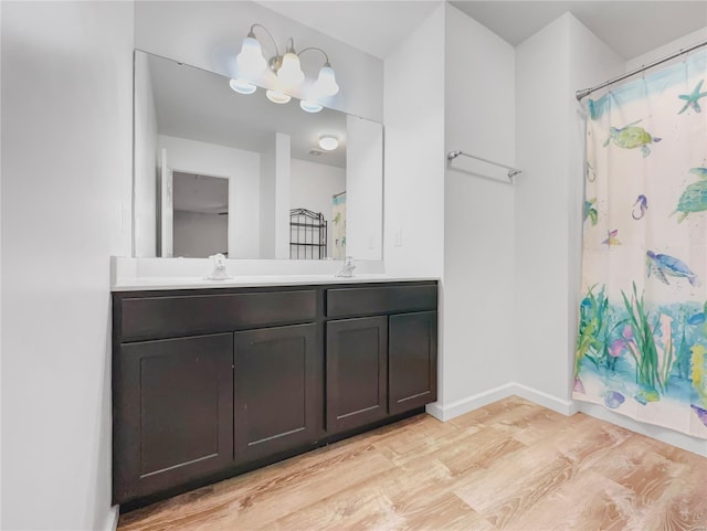 full bath with double vanity, wood finished floors, a sink, baseboards, and a shower with shower curtain