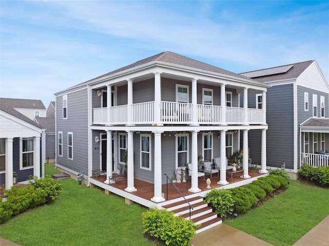 rear view of house with a lawn, covered porch, roof with shingles, and a balcony