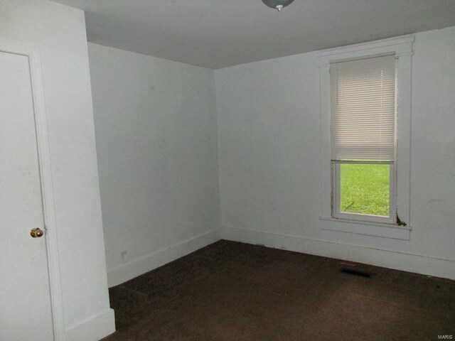 empty room featuring baseboards, visible vents, and dark carpet