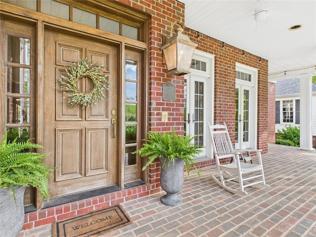 view of exterior entry featuring covered porch and brick siding