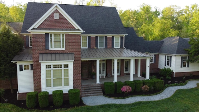view of front facade featuring brick siding, a shingled roof, covered porch, and a standing seam roof