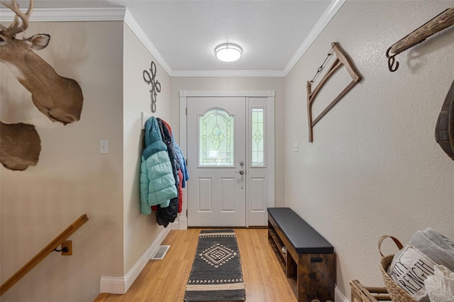 entryway with baseboards, ornamental molding, light wood-style flooring, and visible vents