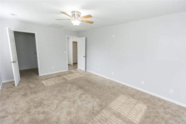 unfurnished bedroom featuring ceiling fan, light colored carpet, a walk in closet, baseboards, and visible vents