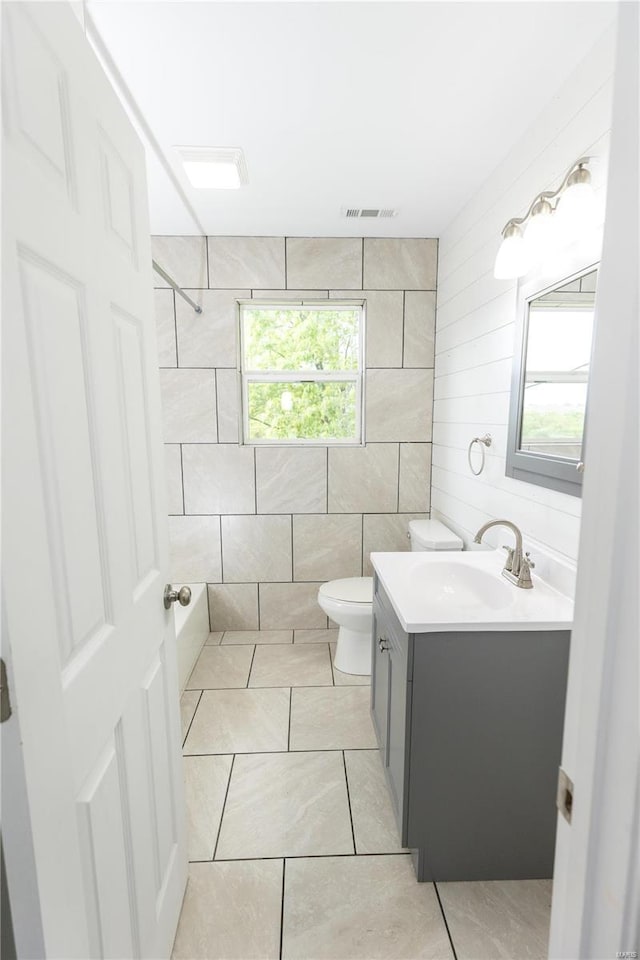 bathroom featuring vanity, walk in shower, toilet, and tile walls