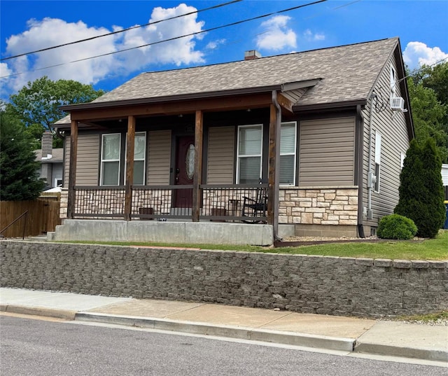 view of front of property featuring a shingled roof, covered porch, and stone siding