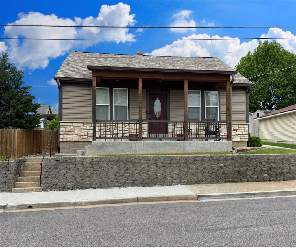 bungalow with fence, a shingled roof, stone siding, stairway, and covered porch