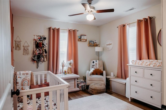bedroom featuring visible vents, a ceiling fan, a crib, and wood finished floors