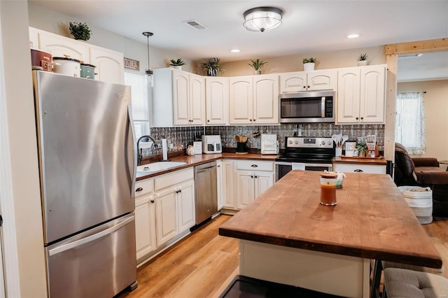 kitchen featuring stainless steel appliances, wood counters, decorative backsplash, and a sink