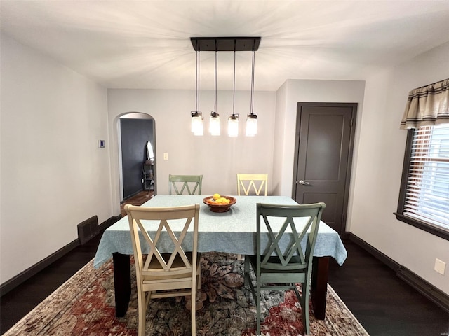 dining space featuring arched walkways, baseboards, dark wood-type flooring, and visible vents