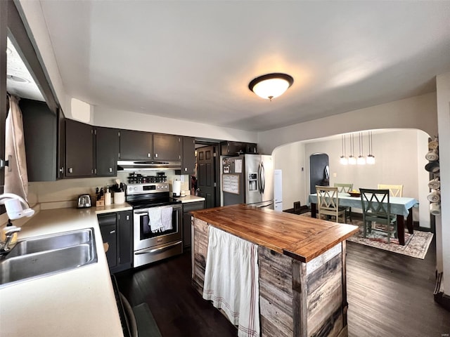 kitchen featuring a sink, under cabinet range hood, arched walkways, dark wood-style floors, and appliances with stainless steel finishes