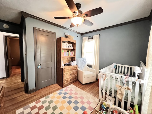 bedroom featuring a ceiling fan, a nursery area, crown molding, and wood finished floors