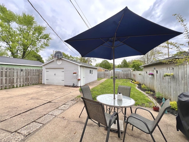 view of patio / terrace featuring a garage, concrete driveway, an outdoor structure, outdoor dining area, and a fenced backyard