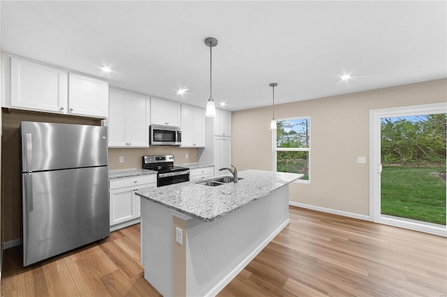 kitchen featuring appliances with stainless steel finishes, a sink, light wood-style floors, white cabinetry, and a center island with sink