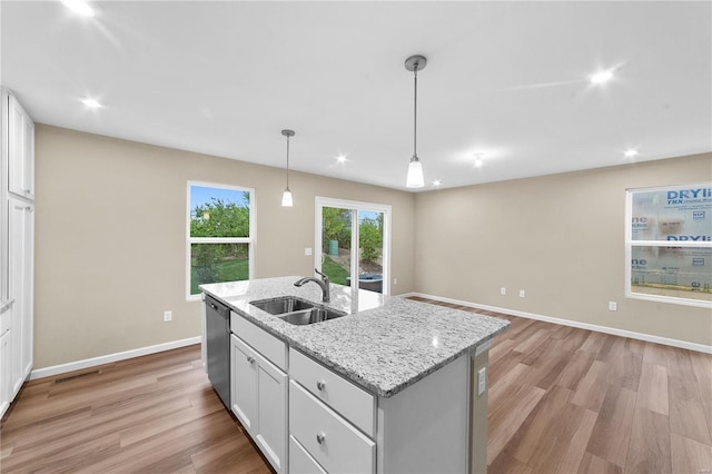 kitchen featuring stainless steel dishwasher, an island with sink, white cabinetry, a sink, and light wood-style flooring