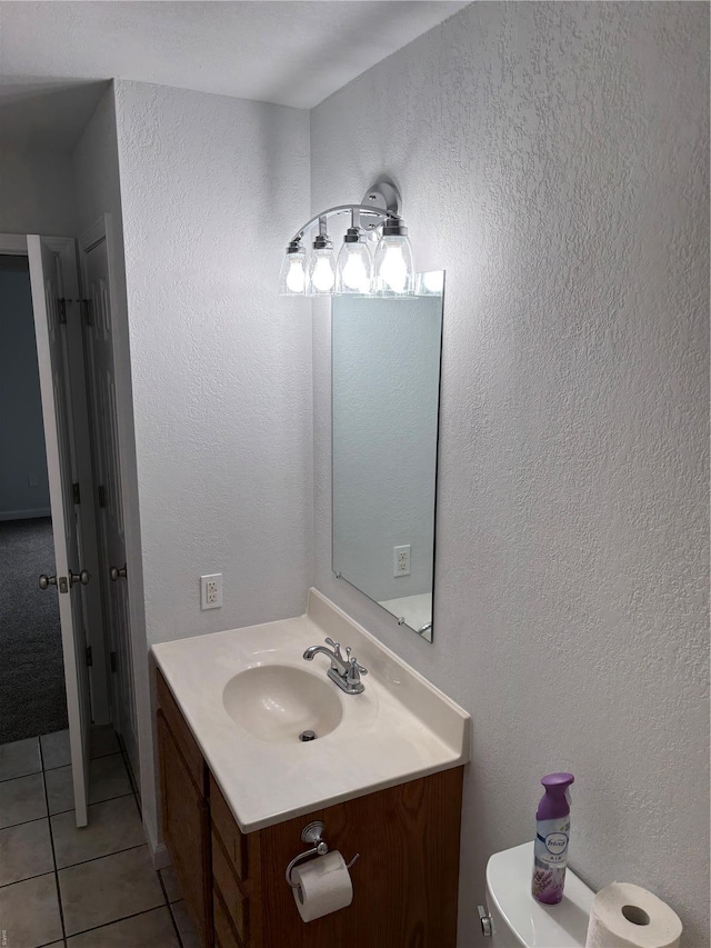 bathroom with toilet, a textured wall, tile patterned flooring, and vanity