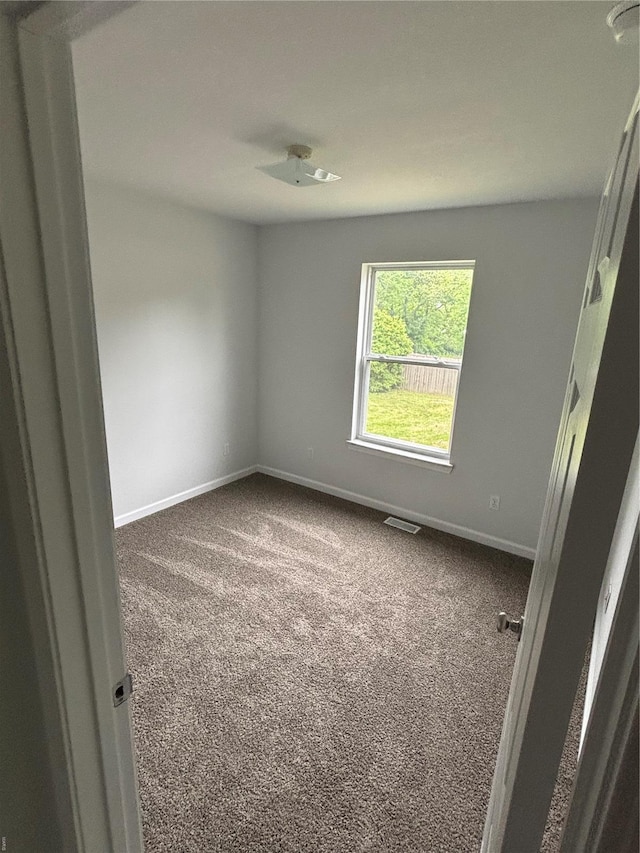 empty room featuring baseboards, dark carpet, and visible vents